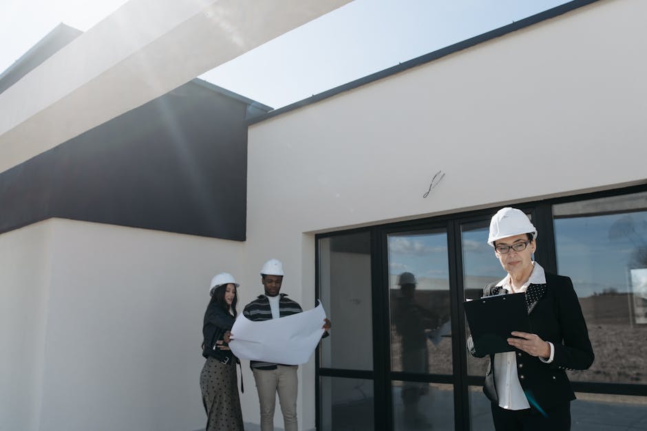 Real estate professionals wearing helmets review building plans at a modern construction site.